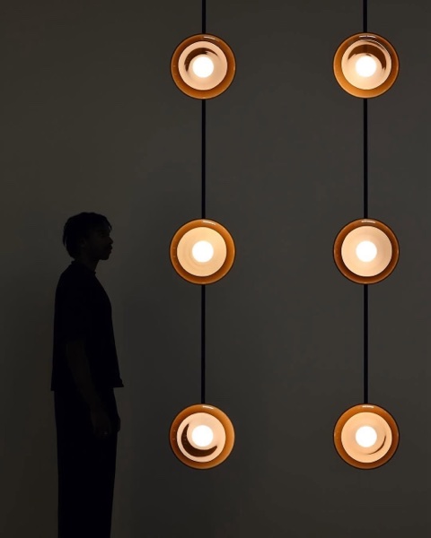 A figure in silhouette facing two columns of glowing pendant lamps
