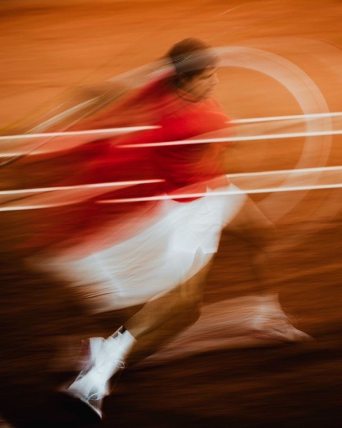 A player in red and white blurred mid-stride across a clay court